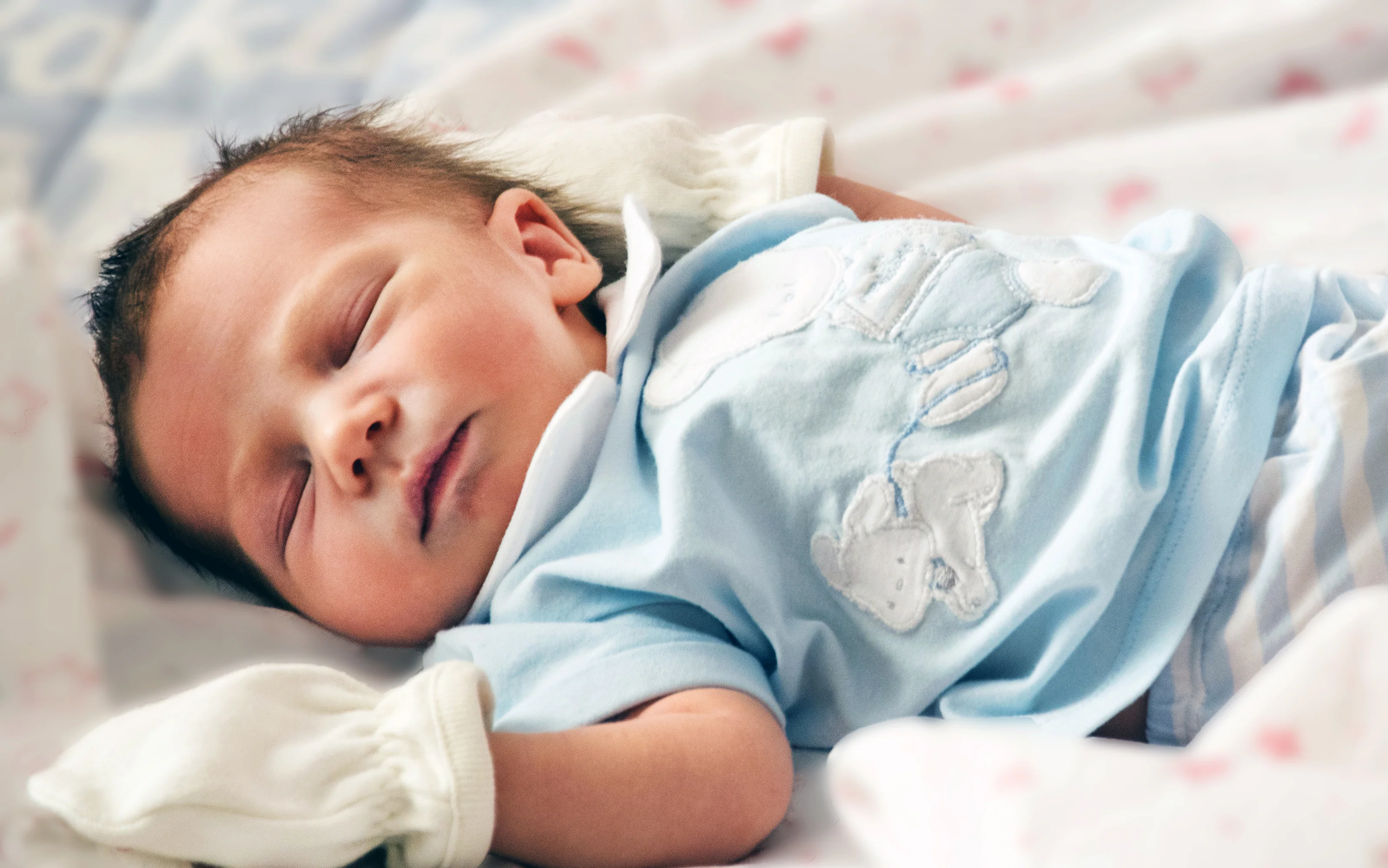 A peaceful sleeping newborn baby in a light blue onesie